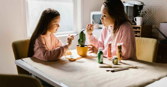 A mother and daughter painting something at a desk.