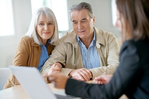 A woman points at a laptop while speaking to an older man and woman.