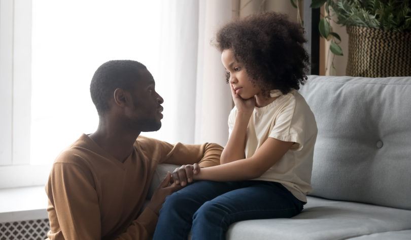 Man kneeling, talking to a young girl sitting on the couch.